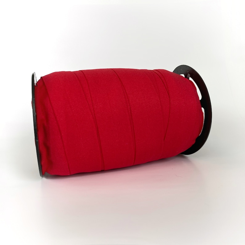 Peut inclure: Un rouleau de ruban &eacute;lastique rouge enroul&eacute; autour d'une bobine en plastique noire.