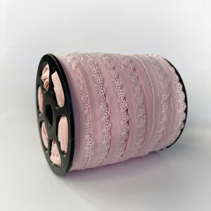 May include: A spool of pink elastic lace trim with a scalloped edge. The trim is wound around a black plastic spool.