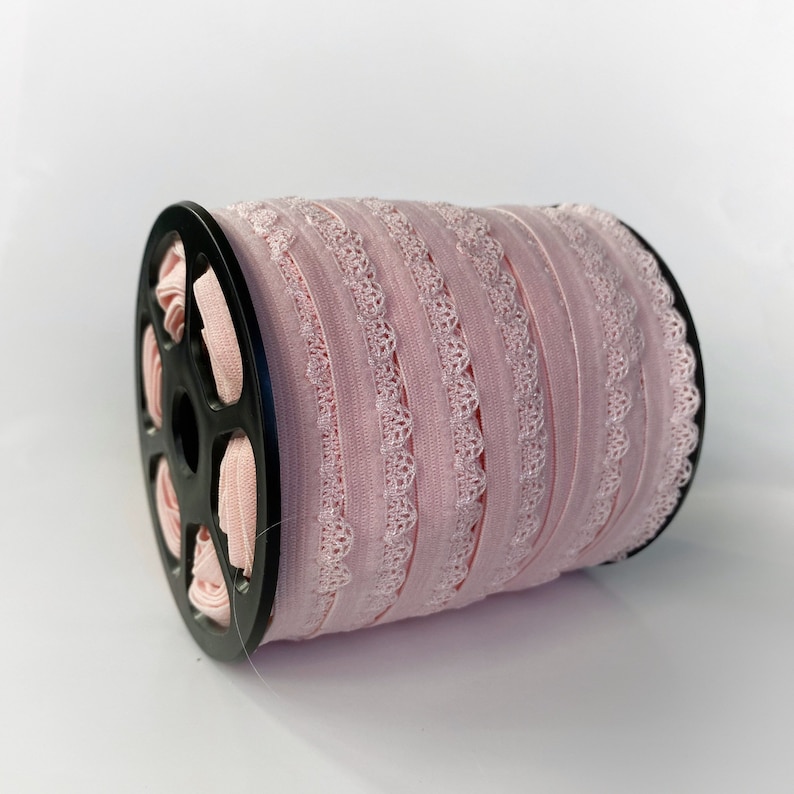 May include: A spool of pink elastic lace trim with a scalloped edge. The trim is wound around a black plastic spool.