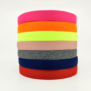 May include: A stack of seven colourful elastic bands in various colours, including pink, orange, yellow, beige, grey, navy blue, and red.