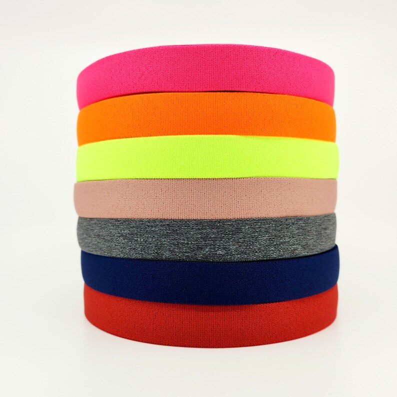 May include: A stack of seven colourful elastic bands in various colours, including pink, orange, yellow, beige, grey, navy blue, and red.