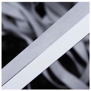 May include: A close-up of a white and gray reflective tape. The tape is made of a thin, flexible material and has a smooth, shiny surface.