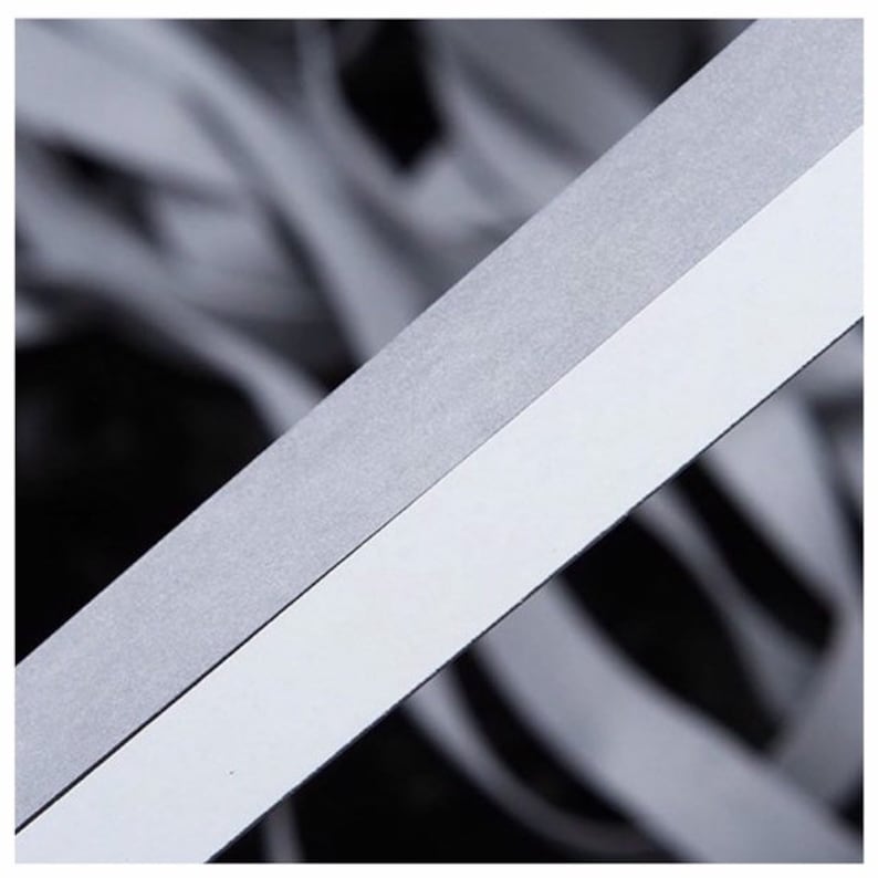 May include: A close-up of a white and gray reflective tape. The tape is made of a thin, flexible material and has a smooth, shiny surface.