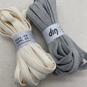 May include: Two spools of cotton cord, one white and one grey. The white spool has a label that reads "Fashion Supplies" and "din fashionsupplie". The grey spool has a label that reads "din".