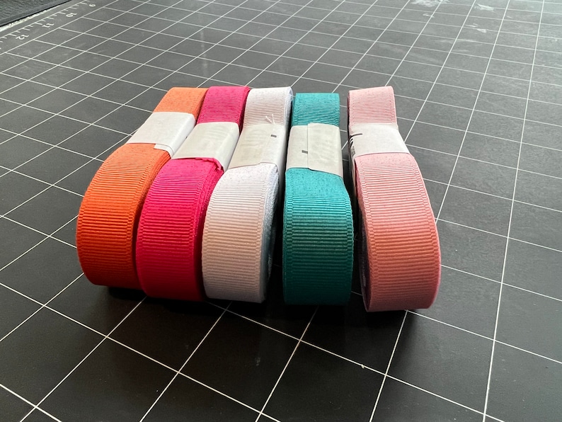 May include: Five spools of ribbon in various colors, including orange, pink, white, teal, and blush.
