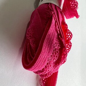 May include: Pink elastic trim with a lace design. The trim is rolled up and secured with a white label that says "Flip".