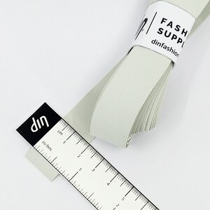 May include: A roll of light grey elastic ribbon measuring 12.7 cm long. The ribbon is folded and has a white label with the text "FASH SUPP dinfashion".