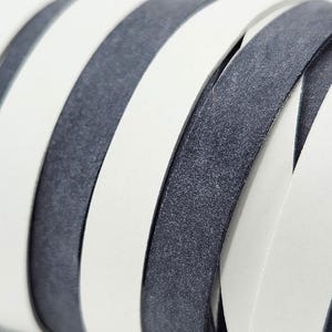 May include: Close-up of a woven leather strap with alternating white and dark gray stripes. The leather has a textured surface.