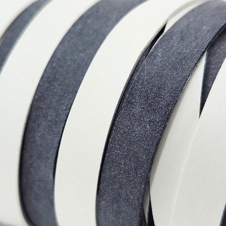 May include: Close-up of a woven leather strap with alternating white and dark gray stripes. The leather has a textured surface.