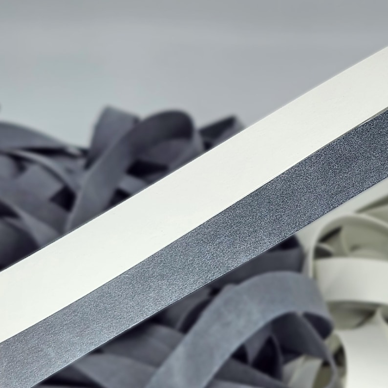 May include: A close-up of a white and gray fabric tape. The tape has a textured surface and is folded in half.