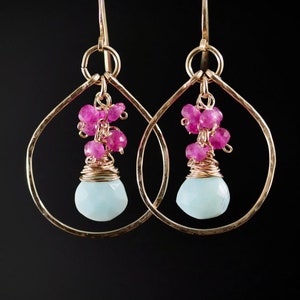 May include: Gold hoop earrings with a teardrop-shaped aquamarine gemstone and pink beads dangling from the bottom.