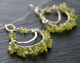 May include: Gold earrings with a double hoop design, adorned with green peridot gemstones.