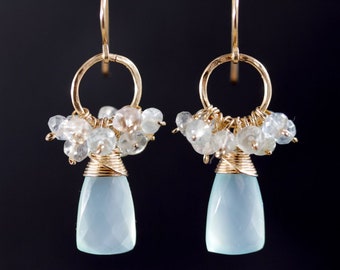 May include: Gold earrings with a teardrop-shaped blue chalcedony gemstone and a cluster of small white and blue crystals.