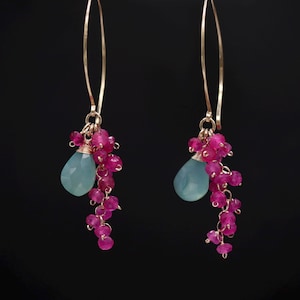 May include: A pair of dangle earrings featuring long gold-toned ear wires. Each earring is adorned with a cluster of small, round, vibrant pink beads and a single, larger, faceted, teardrop-shaped light blue stone suspended from a gold ring.