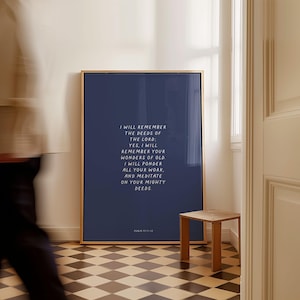 May include: A framed navy blue print with gold trim, featuring white text that reads "I WILL REMEMBER THE DEEDS OF THE LORD..." A small wooden side table sits to the right. The floor has a black and white checkered pattern.