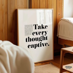May include: A framed print with the text "Take every thought captive" in a bold, black font. The print also includes a passage from 2 Corinthians 10:3-6. The frame is a light wood color, and the background is a bedroom setting.