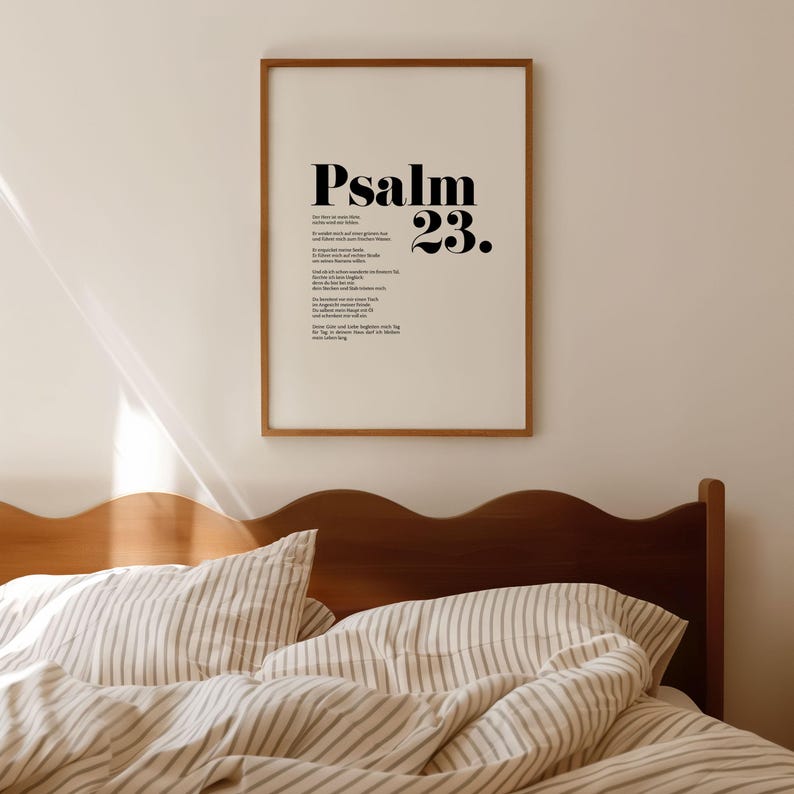 May include: A framed print with a white background and black text. The text reads "Psalm 23." The print is hanging on a white wall above a wooden bed with striped bedding.