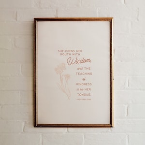 May include: A framed print with a white background and a brown floral design. The text reads "She opens her mouth with Wisdom, and the teaching of kindness is on her tongue. Proverbs 31:26"