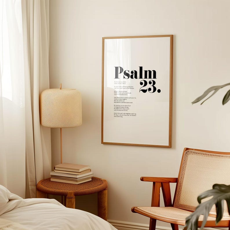 May include: A framed print with a white background and black text that reads "Psalm 23." The print is hanging on a white wall in a room with a wooden chair, a lamp, and a side table.
