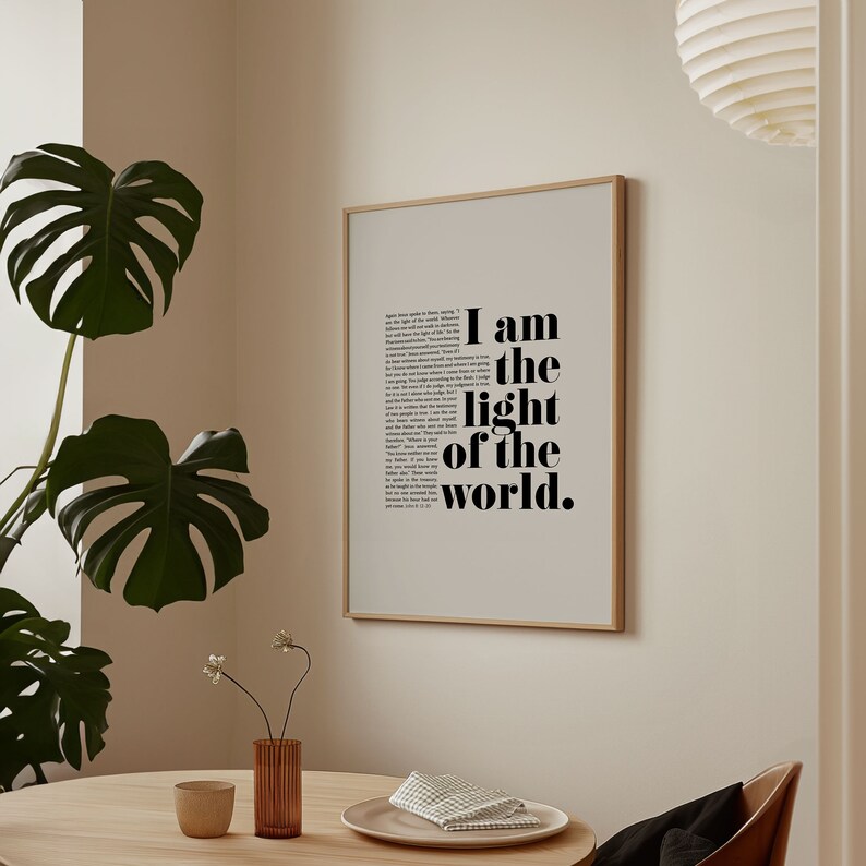 K&ouml;nnte beinhalten: Ein gerahmter Druck mit wei&szlig;em Hintergrund und schwarzem Text, der "Ich bin das Licht der Welt" lautet. Der Druck h&auml;ngt an einer hellbeigen Wand.
