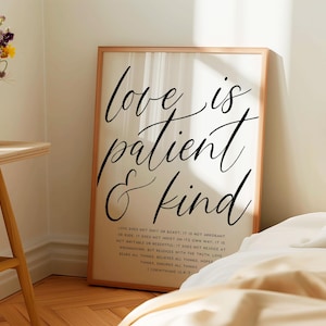 Op de afbeelding: Een ingelijst print met een witte achtergrond en zwarte tekst die "love is patient & kind" luidt. De tekst is in een cursief schrift. Onder de tekst staat een citaat uit de Bijbel, 1 Korintiërs 13:4-7.