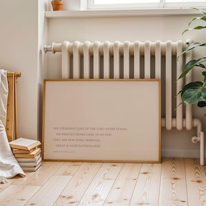 May include: A framed print with a light beige background and a wooden frame. The text in the print reads, "THE STEADFAST LOVE OF THE LORD NEVER CEASES, HIS MERCIES NEVER COME TO AN END, THEY ARE NEW EVERY MORNING, GREAT IS YOUR FAITHFULNESS."