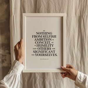 Puede incluir: Impresión enmarcada en blanco con texto negro. El texto dice: "No hagan nada por egoísmo o vanidad, sino con humildad, consideren a los demás como más importantes que ustedes mismos." Filipenses 2:3.