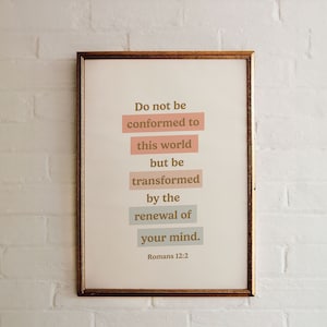 May include: A framed print with a white background and gold frame. The print features a quote from the Bible, Romans 12:2, in brown text: "Do not be conformed to this world, but be transformed by the renewal of your mind."