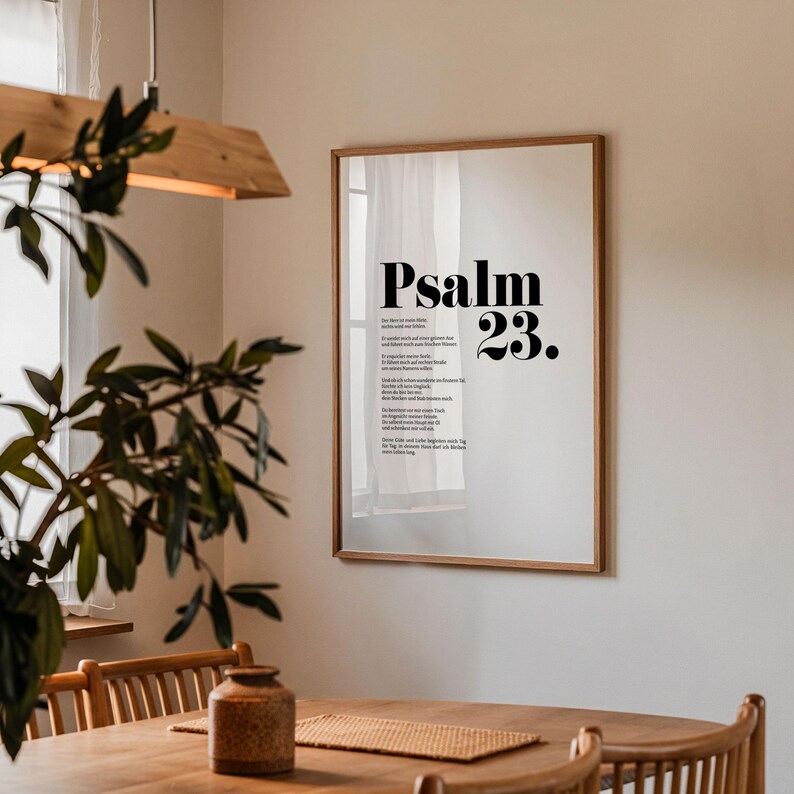 May include: A framed print with a white background and black text. The text reads "Psalm 23." The print is hanging on a white wall in a room with a wooden table and chairs.