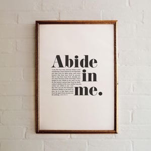 May include: A framed print with a white background and black text that reads "Abide in me." The text is in a bold, sans-serif font. The quote is from the Bible, John 15:4-5.