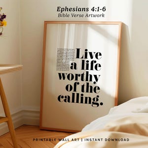 May include: A framed print with the text "Live a life worthy of the calling" in bold black letters. The artwork is a Bible verse from Ephesians 4:1-6. The print is in a light-colored wooden frame and is displayed in a room with a neutral color palette.