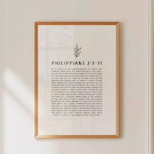 Könnte beinhalten: Ein gerahmter Druck mit weißem Hintergrund und schwarzem Text. Der Text ist ein Bibelvers aus Philipper 2:1-11. Der Druck hat ein schlichtes, minimalistisches Design mit einer kleinen Blattillustration oben.