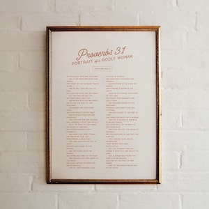 Op de afbeelding: Een ingelijst afdruk met een witte achtergrond en een gouden lijst. De afdruk bevat de tekst "Spreuken 31: Portret van een godvruchtige vrouw" in een cursief lettertype. De tekst is lichtroze van kleur. De tekst gaat verder met een lijst van eigenschappen van een godvruchtige vrouw, ook in lichtroze.