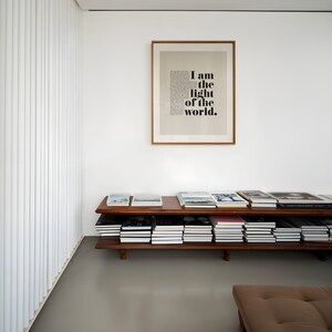K&ouml;nnte beinhalten: Ein B&uuml;cherregal aus Holz mit zwei Regalbrettern, gef&uuml;llt mit B&uuml;chern. Das Regal steht an einer wei&szlig;en Wand mit einem gerahmten Druck, auf dem "Ich bin das Licht der Welt" steht.