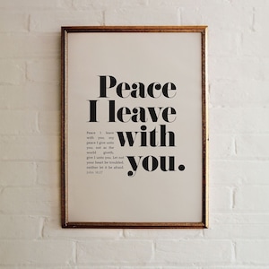 May include: A framed print with the words "Peace I leave with you." in bold black font. The print includes a quote from John 14:27. The frame is gold-colored, and the background is a white brick wall.