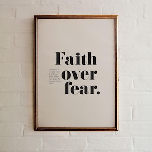 Puede incluir: Una impresión enmarcada con fondo blanco y texto negro que dice "Faith over fear." El texto está en negrita, sin serif. La cita es del Salmo 27:1.
