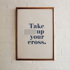 Könnte beinhalten: Ein gerahmter Druck mit weißem Hintergrund und goldenem Rahmen. Der Druck zeigt den Text "Take up your cross." in dunkelblau.