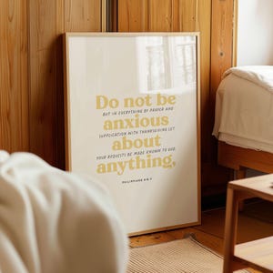 Op de afbeelding: Een beige poster met een gouden lijst heeft een gele tekstoverlay met de tekst "Wees in geen ding bezorgd, maar laat in alles door gebed en smeking met dankzegging uw verzoeken bekend worden bij God, Filippenzen 4:6-7".