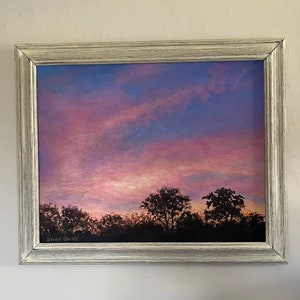 Op de afbeelding: Een ingelijst schilderij van een roze en paarse zonsondergang met silhouetbomen op de voorgrond. Het schilderij is onderaan links gesigneerd met "Gwen Howell".