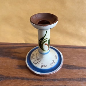 Puede incluir: Un portavelas de cerámica blanca con la parte superior marrón y la base azul. La base tiene el texto "In Bermuda called but few sew get up".