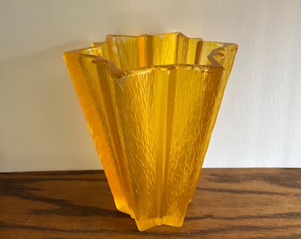 May include: A yellow glass vase with a star-shaped opening and a textured surface.