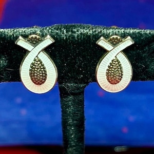 Peut inclure: Une paire de boucles d'oreilles en émail blanc et noir avec un motif géométrique. Les boucles d'oreilles sont de forme ovale et ont une couleur argentée.