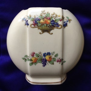 May include: A white ceramic vase with a rounded shape and a gold trim. The vase is decorated with a floral pattern featuring fruit and leaves in shades of red, green, blue, and yellow.