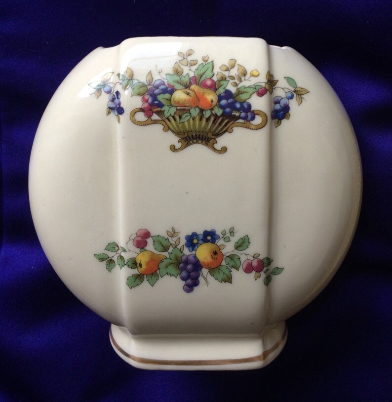May include: A white ceramic vase with a rounded shape and a gold trim. The vase is decorated with a floral pattern featuring fruit and leaves in shades of red, green, blue, and yellow.