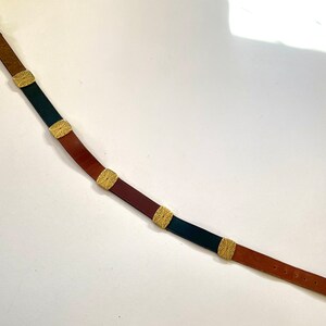 May include: A brown leather belt with a gold buckle and decorative metal accents. The belt has alternating sections of brown and black leather.