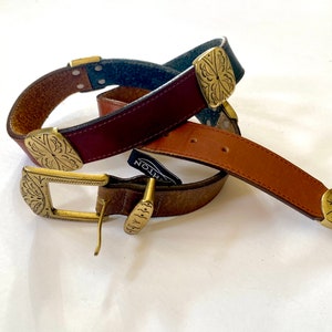 May include: Two leather belts with ornate brass buckles. The belts are brown, tan, and dark blue. The buckles have a floral design.