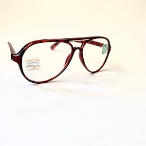 May include: A pair of vintage-style eyeglasses with a dark red tortoiseshell frame. The lenses are clear, and there are small stickers on the lenses with text. The glasses have a classic aviator shape.