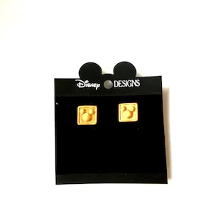 May include: A pair of gold Mickey Mouse head earrings on a black card with the text "Disney Designs".