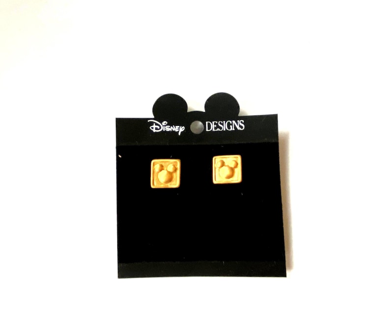 May include: A pair of gold Mickey Mouse head earrings on a black card with the text "Disney Designs".