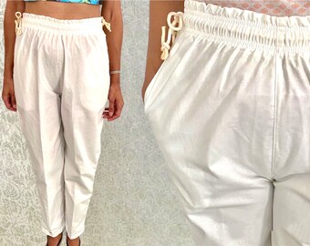 May include: White cotton pants with a drawstring waist and elastic waistband. The pants have a relaxed fit and are cropped at the ankle.